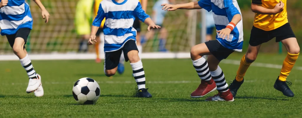 crianças jogando bola em uma quadra com grama sintética